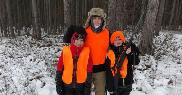 Three young hunters wearing orange stand ready for youth hunting