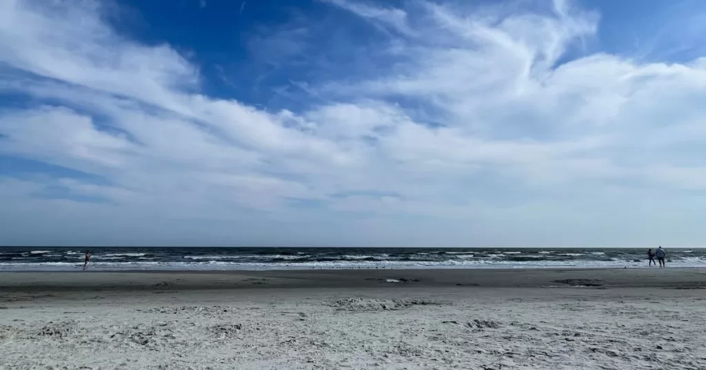 A blue and cloudy sky on the beach after sunrise with a view of each waves and sand