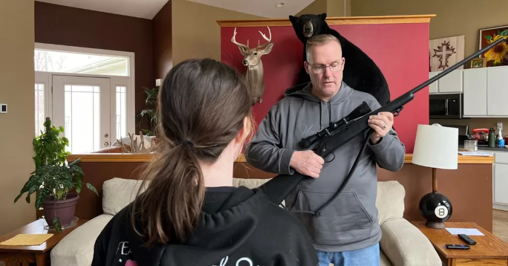 Hunter holding a rifle and with young girl watching proper safety handling.
