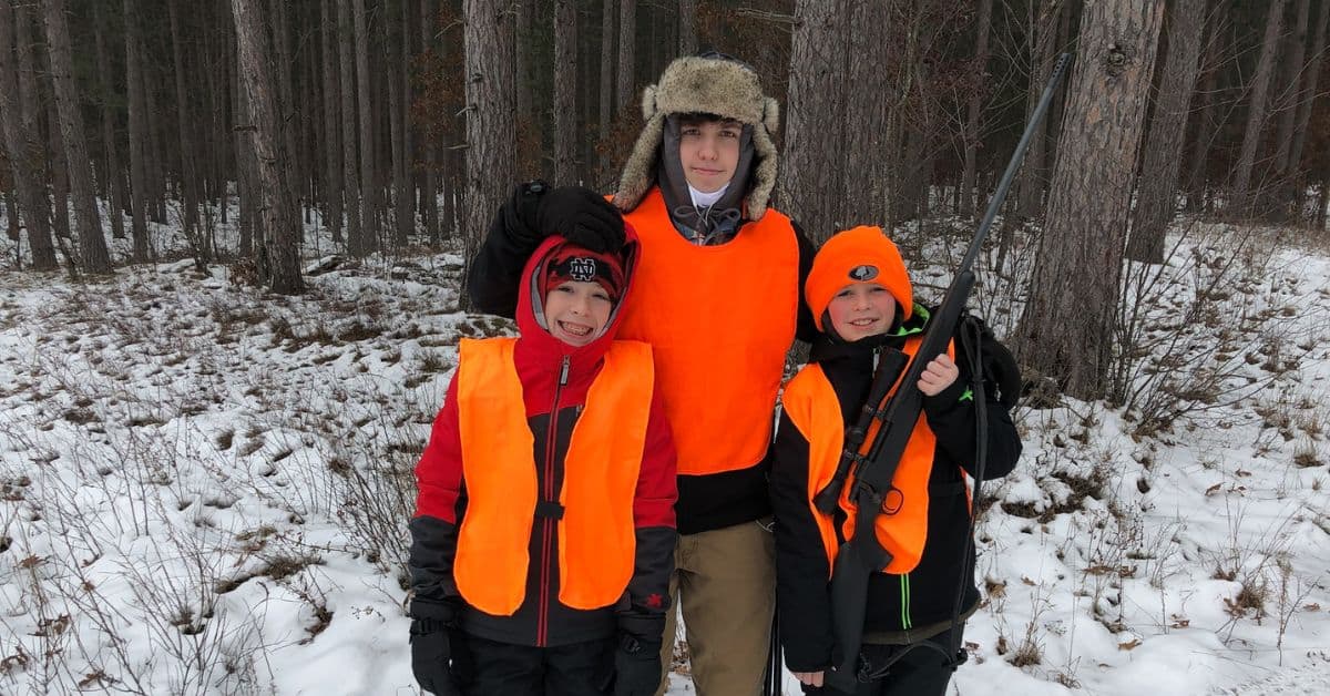 Three young hunters wearing orange stand ready for youth hunting