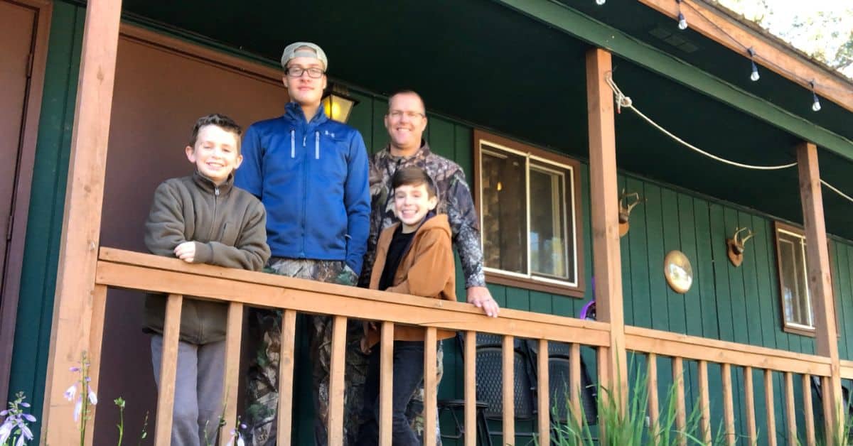Father and sons standing outside campground cabin on the porch leaning on the railing.