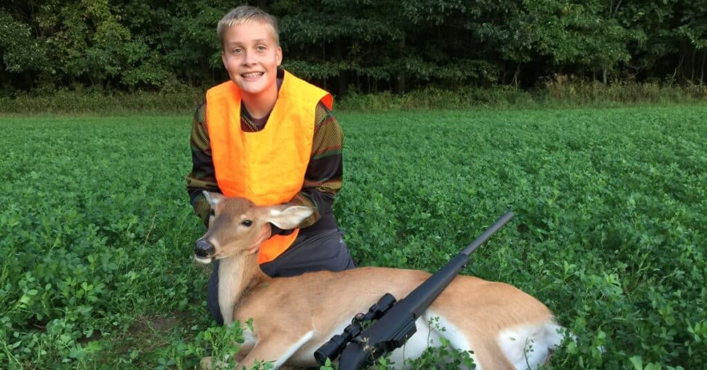 A young hunter wearing orange and posing by his first deer.