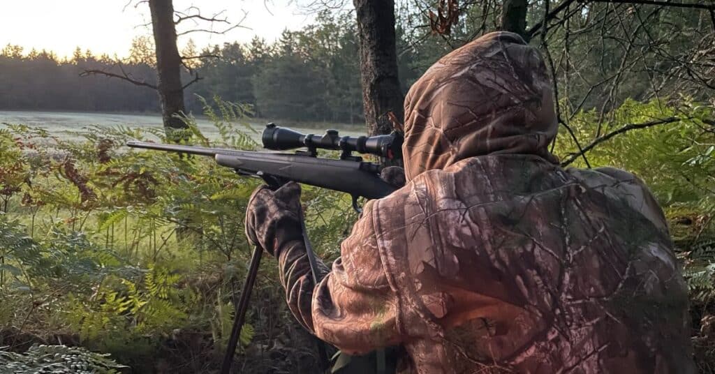 Hunter in camouflage aiming a rifle at a deer