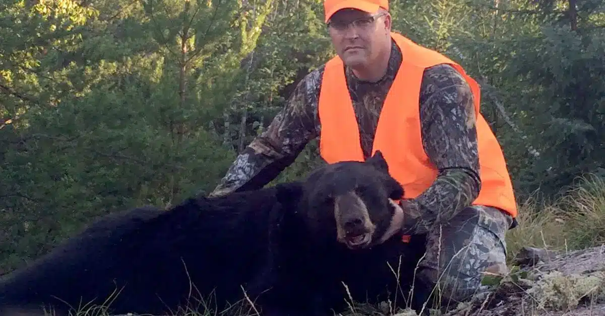 Hunting wearing camouflage and orange sitting near his black bear hunt