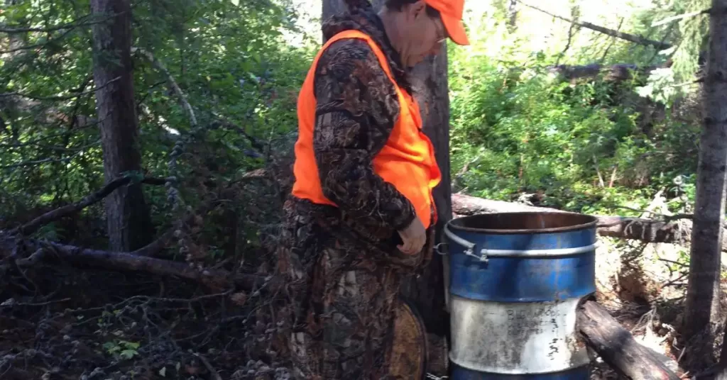 Guide setting up bear bait by large tub in woods