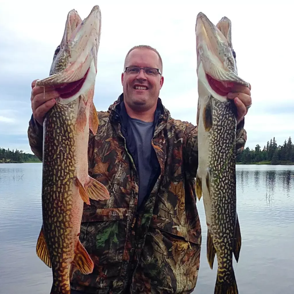 Hunter holding two northern pike in front of lake