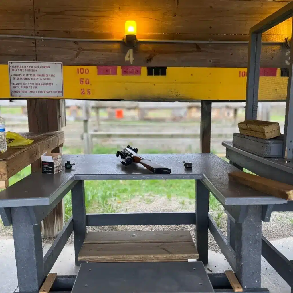 A view of a firing lane with ammo, bench, table, blocks, rifle and magazine. 