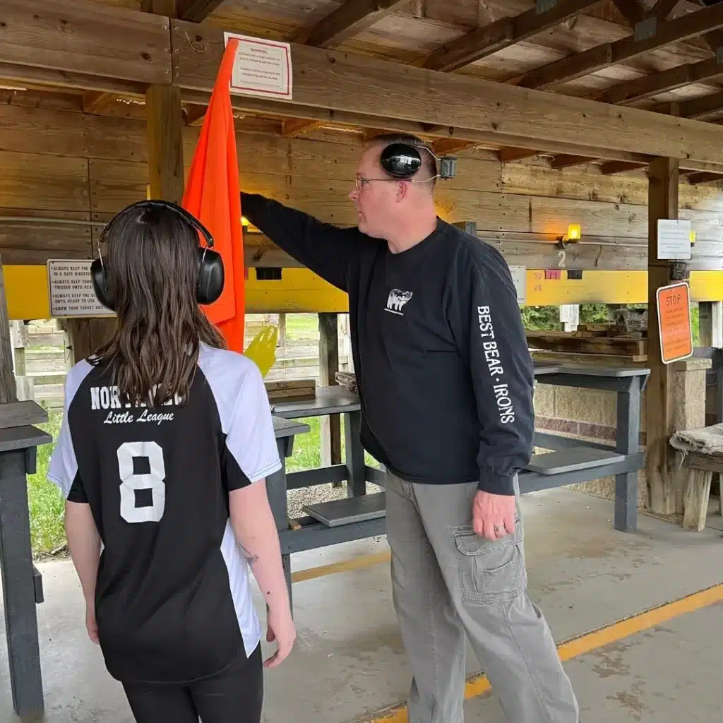 Experienced gunman shows a beginner student how to use the orange safety flag that is hung on a wall