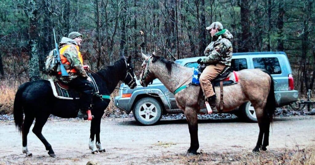 Two hunters on horseback in the woods