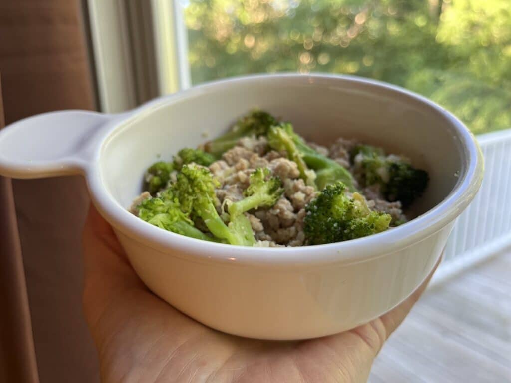 a small white bowl of ground turkey, seasonings and topped with green broccoli