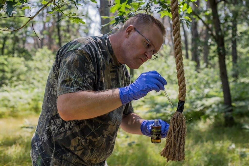 Hunter applying buck lure to rope hanging from tree with a dropper