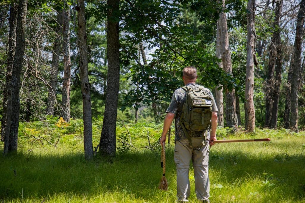 Hunter wearing camo and backpack standing in forest while carrying a rope.