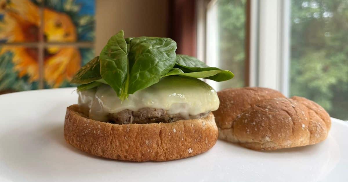 An open-faced turkey burger on a bun with cheese and spinach.