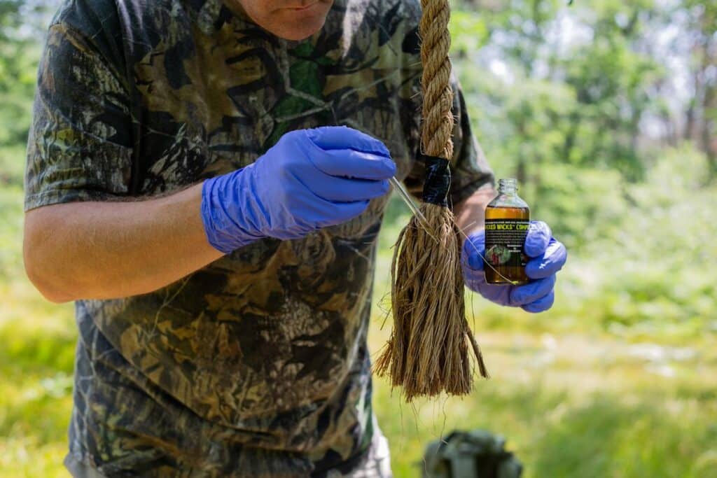 Hunter in the woods applying deer lure liquid to manila rope for mock scrape