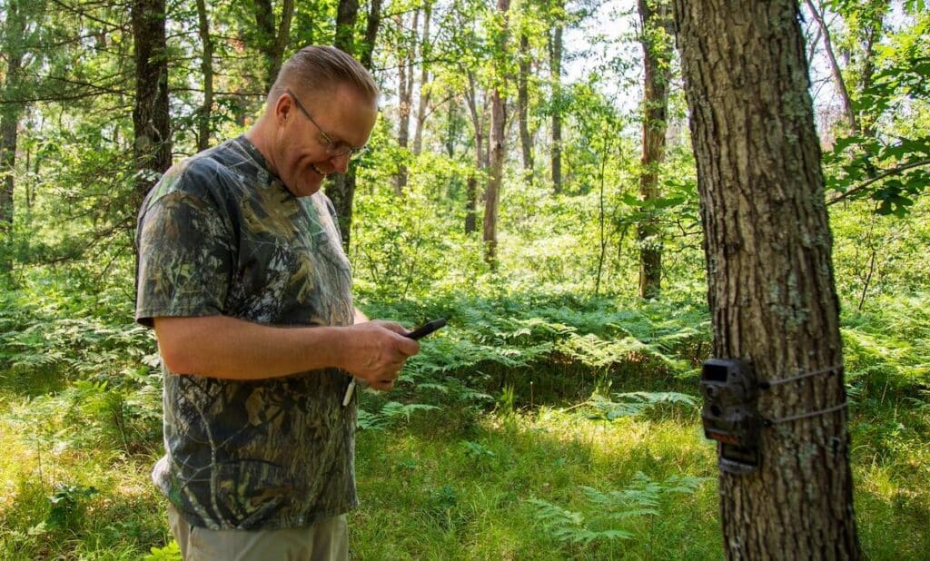 Happy hunter standing in the woods and looking at photos on his smartphone